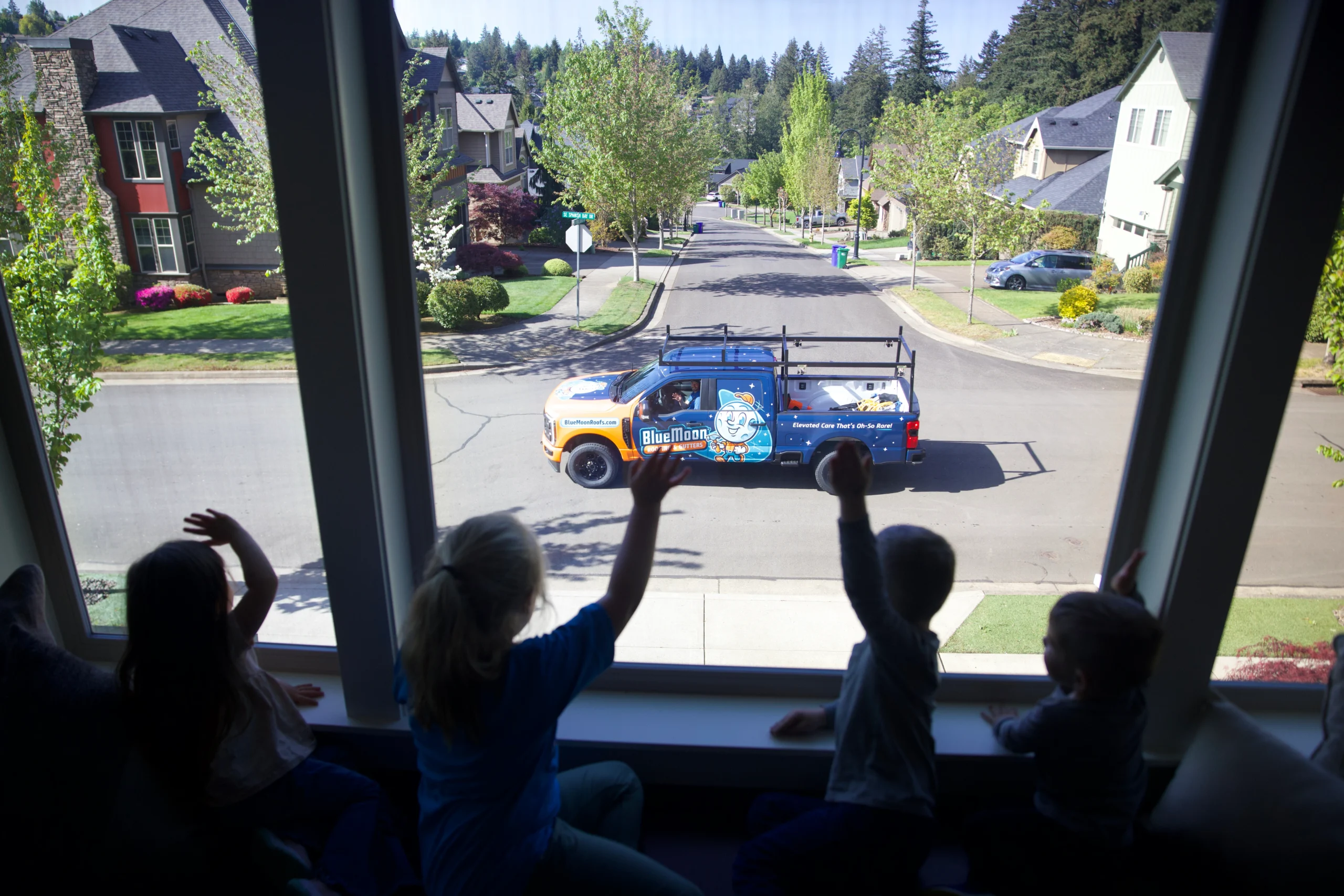 Kids waving to a blue moon roofs truck