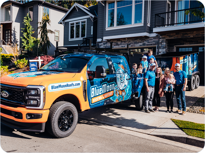 Meet the Team: A Blue Moon Roofing & Gutters truck is parked in front of a house, with a group of people posing and smiling beside it.