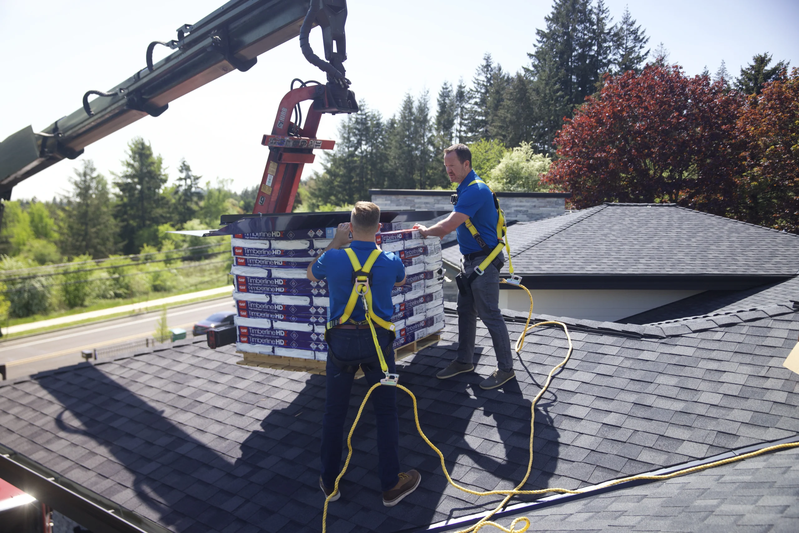 Two workers unloading shingles onto a roof from a crane.