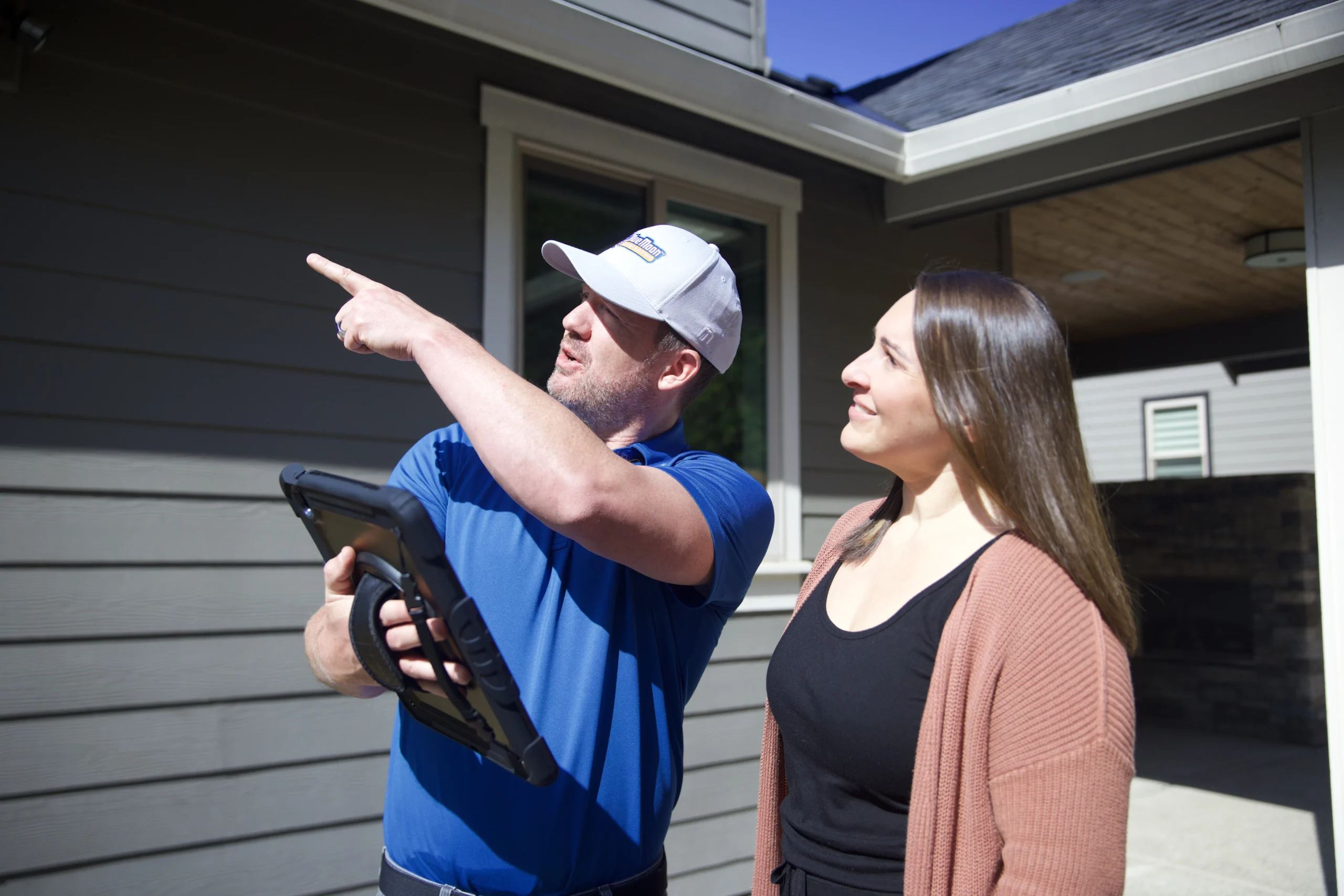 Man pointing out something to a woman about her roof.