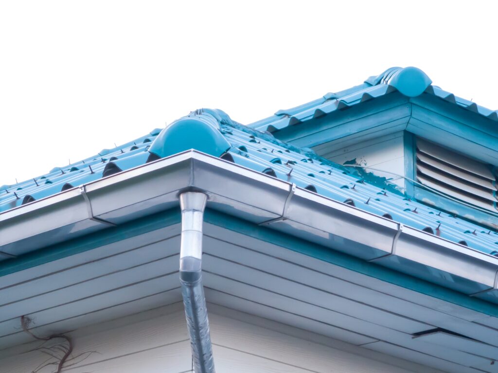 Close-up of a house roof with blue tiles, featuring seamless gutters and a ventilated attic window, set against a white sky—an ideal feature for many Portland homes.