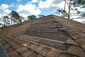 A house roof in Portland with missing shingles exposing the underlayment, showing signs of storm or wind damage—ideal for roof repair or roof replacement. Trees and a partly cloudy sky frame the scene.