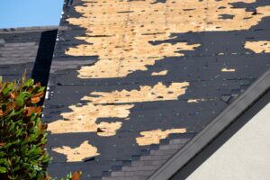 A house roof in Portland with large sections of missing shingles, exposing plywood underneath, signals the urgent need for roof repair or even roof replacement after significant storm or wind damage.
